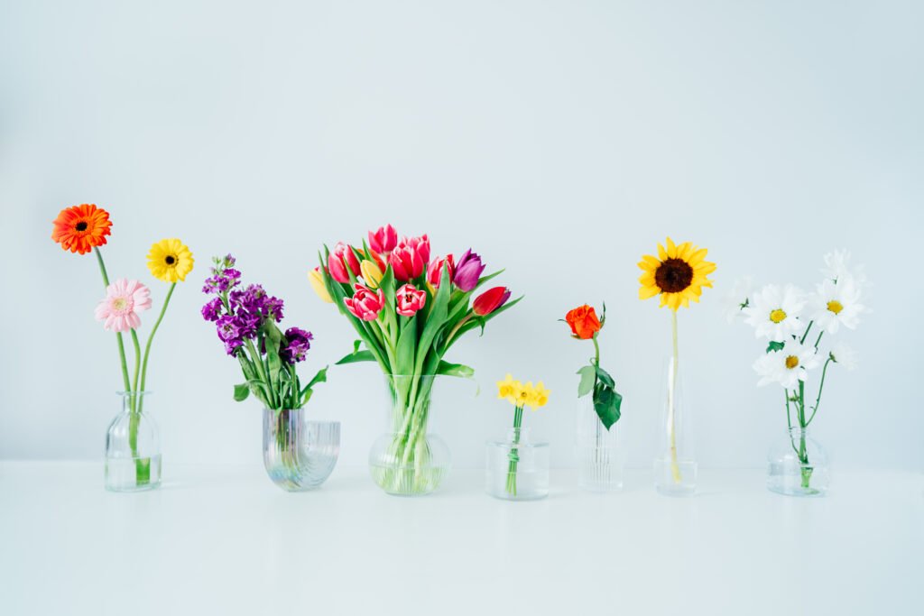 Variation of different flowers in glass vases on white table. Colorful flower arrangement or decoration in rainbow colors. Floristy, making bouquets. Flowers delivery. Selective focus. Copy space.